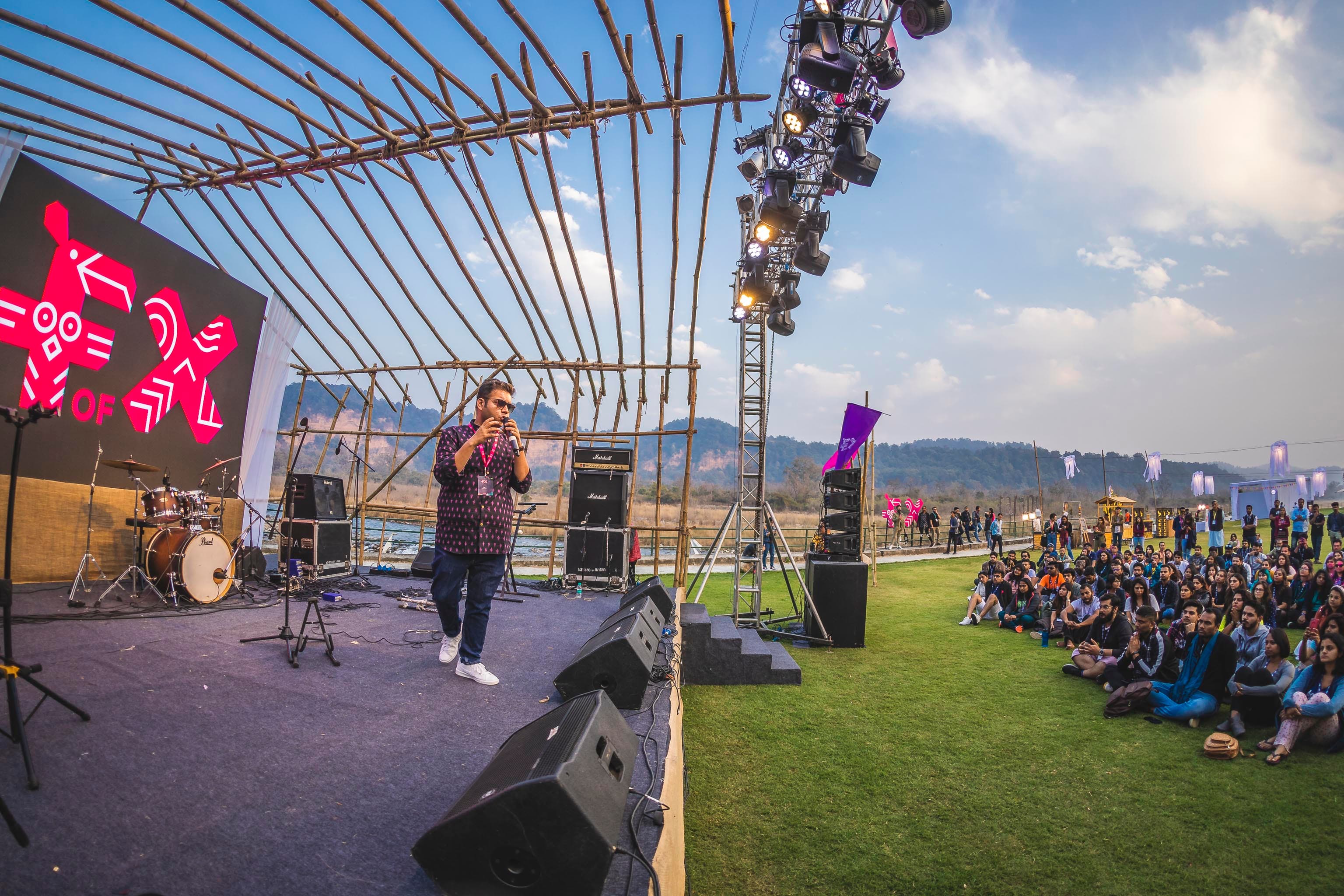 Jay Ahya speaking on an outdoor stage to a seated audience.