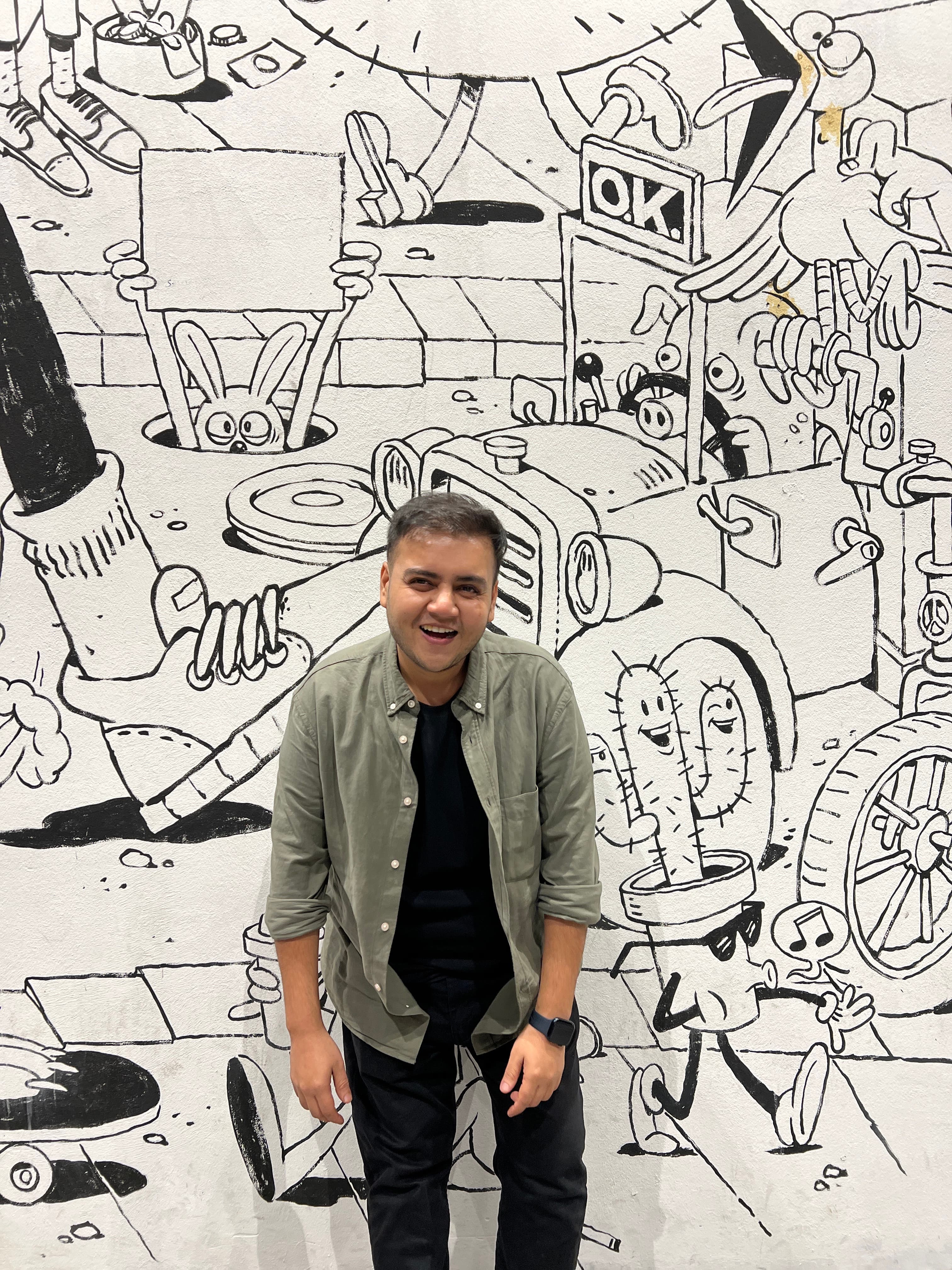 Jay Ahya smiling in front of a black-and-white mural.